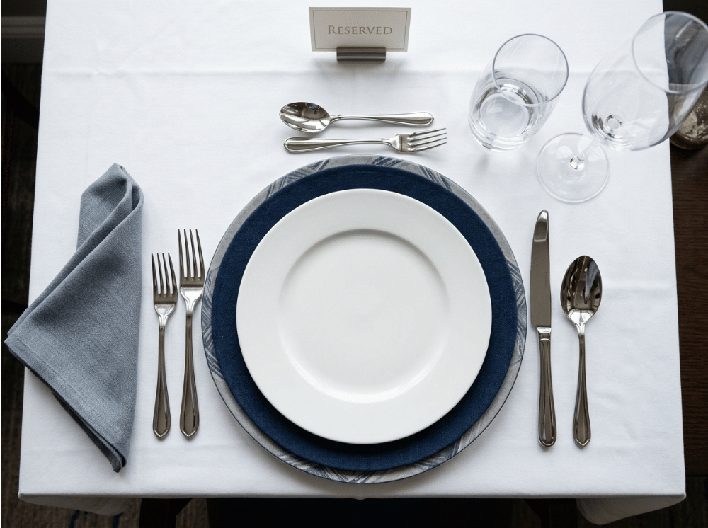 Overhead view of a formal restaurant place setting with polished stainless steel flatware, plate, and glassware. Overhead view of a formal restaurant place setting with polished stainless steel flatware, plate, and glassware.